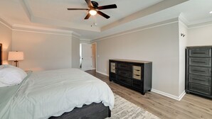 Un dormitorio con cama, cómoda, ventilador de techo y puerta que da a otra habitación.