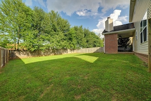 Ein Garten mit Rasenfläche, Holzlattenzaun und gepflasterter Terrasse.