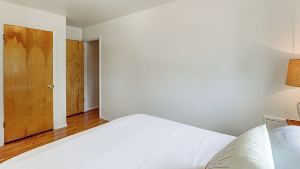 Een slaapkamer met een houten vloer, witte wanden en een bed met witte lakens.