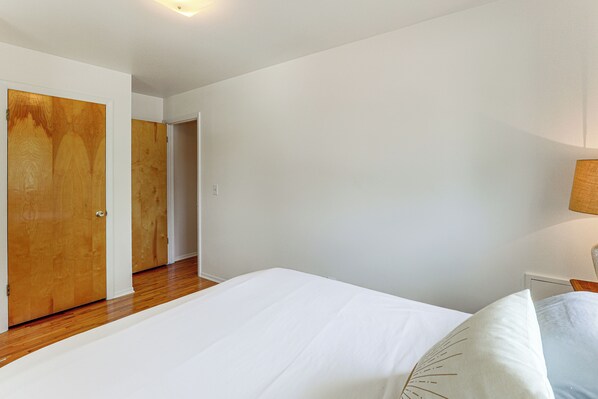 A bedroom with a wooden floor, white walls, and a bed with white bedding.