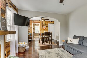 A living room with a grey sofa, a wooden dining table with chairs, a kitchen area with a sign reading 'Kitchen', and a ceiling fan. - 4 Mi to Downtown Columbus! Updated Home w/ Yard (Columbus)