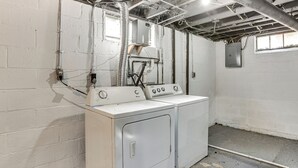Un lavadero con lavadora y secadora blancos, conductos expuestos y una ventana.