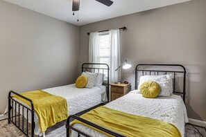A twin bedroom with two beds, a bedside table with a lamp, a window with sheer curtains, and a ceiling fan. - 4 Mi to Downtown Columbus! Updated Home w/ Yard (Columbus)