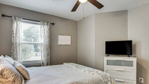 Un dormitorio con cama, televisión en una cómoda y ventana con cortinas.