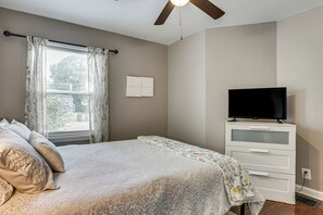 Ein Schlafzimmer mit einem Bett, einem Fernseher auf einer Kommode und einem Fenster mit Vorhängen.