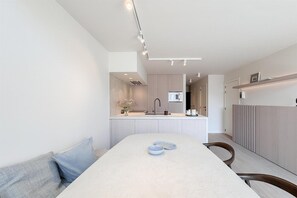 A modern kitchen with a central island, a dining table with chairs, and a built-in bench. - Spacious Duplex in Knokke Centre (KNOKKE)