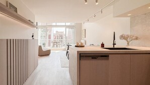Eine moderne Küche mit einer zentralen Kochinsel, ein Essbereich mit einer Couch und Stühlen sowie ein Blick auf die Stadt durch große Fenster.