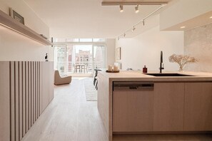 A modern kitchen with a central island, a dining area with a sofa and chairs, and a view of the city through large windows. - Spacious Duplex in Knokke Centre (KNOKKE)