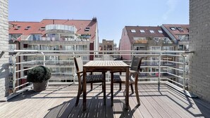 Ein Balkon mit Tisch und Stühlen, mit Blick auf eine Wohngegend mit roten Ziegeldächern.