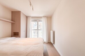 A bedroom with a bed, a radiator, and a window with curtains. - Spacious Duplex in Knokke Centre (KNOKKE)