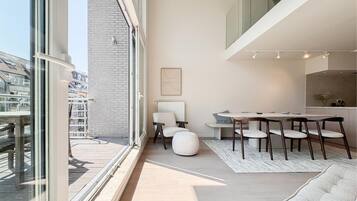 Een modern interieur met een eethoek, een bank en stadszicht door grote ramen.