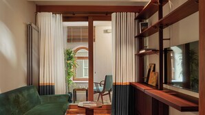 A living room with a green sofa, a small wooden table, a red carpet, a TV on a wooden stand, and a window with curtains. - Nazenin Hotel (Istanbul)