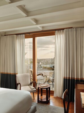 Habitación de hotel con una cama, una mesa redonda, dos sillas, un balcón con vista a la ciudad y cortinas.
