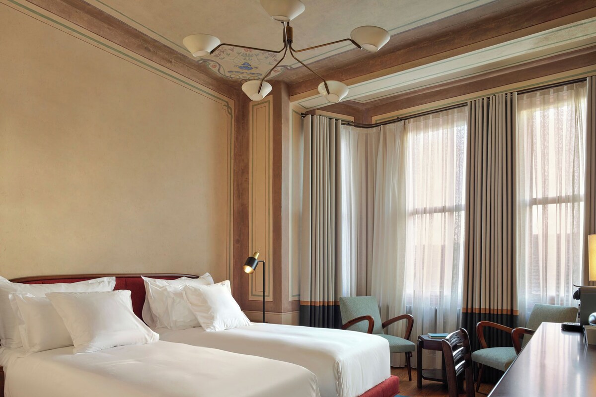 A hotel room with two beds, a dining table, and a chandelier.