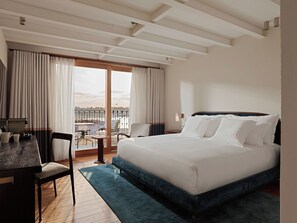 Habitación de hotel con una cama grande, un escritorio con sillas y vistas a la ciudad desde la ventana.