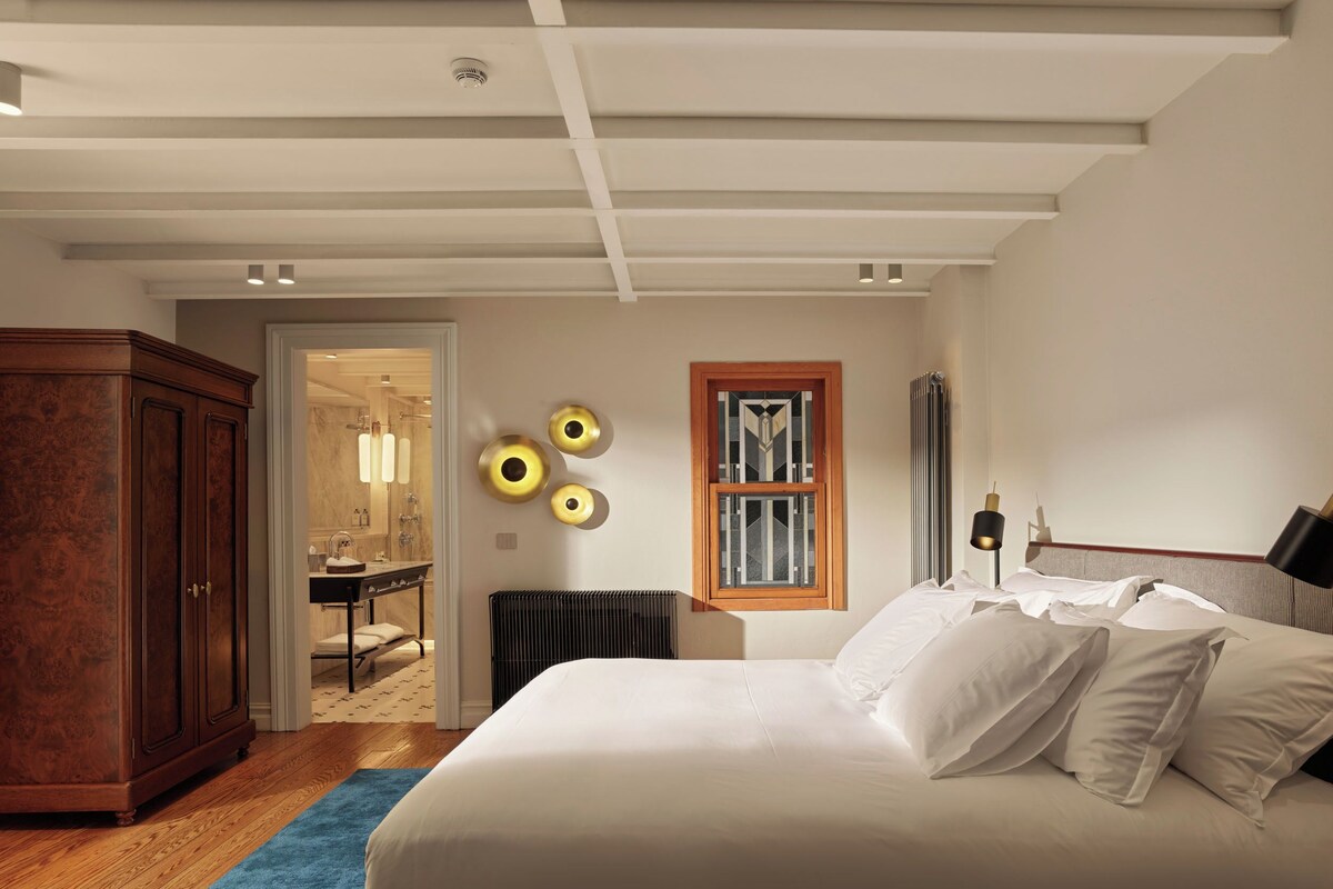 A bedroom with a large bed, a wooden wardrobe, a radiator, and a window with a geometric design.