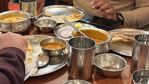 A dining table with multiple metal bowls and plates, some containing food, and a person using a smartphone. - Hotel Smart International (New Delhi)