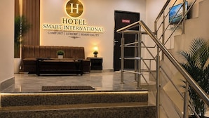 A hotel reception area with a modern staircase, a reception desk, and a sign indicating the hotel's name and services. - Hotel Smart International (New Delhi)