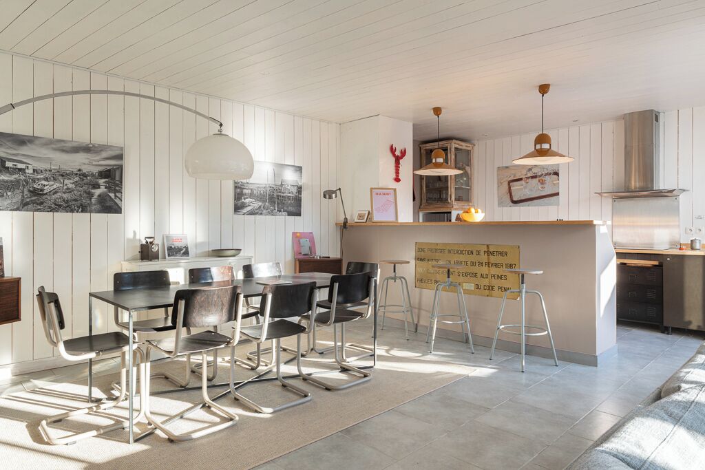Eine moderne Küche mit weißen Schränken, ein Essbereich mit Metallstühlen und eine Bar mit Hockern.