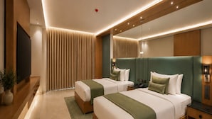 Ein modernes Hotelzimmer mit zwei Betten, einem Flachbildfernseher, einem Nachttisch, einem Spiegel und einer Wandleuchte.