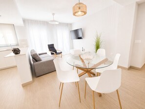 A modern living space with a dining area, a sofa, a TV mounted on the wall, and a plant. - Apartamento la Bodega con piscina (Conil de la Frontera)