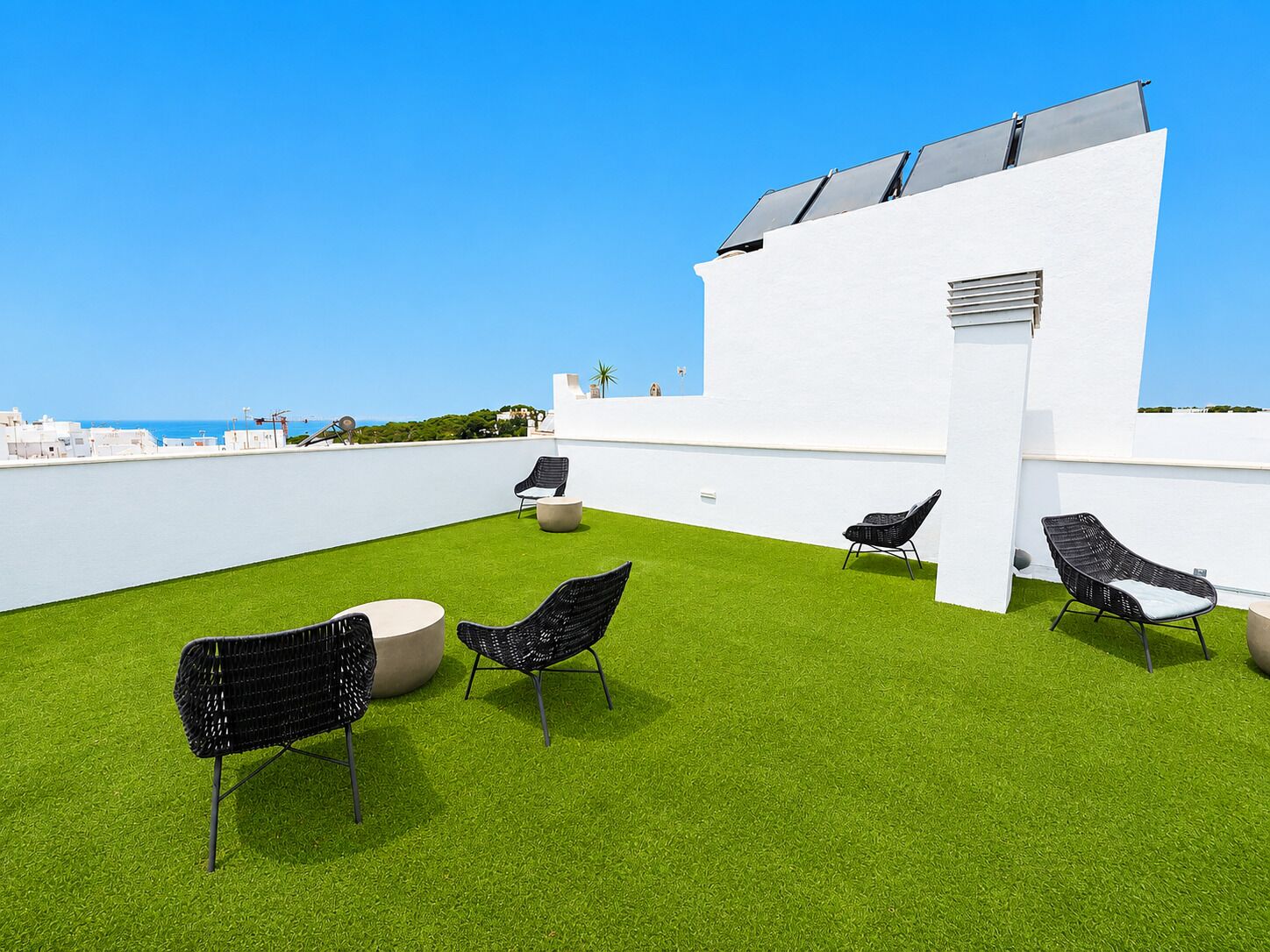 Una terraza en la azotea con césped artificial, mobiliario exterior y un edificio blanco con paneles solares.