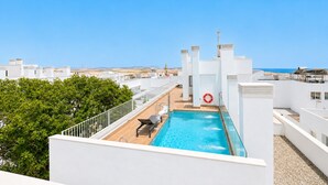 Ein Pool auf dem Dach mit freiem Blick auf das Meer, umgeben von weißen Gebäuden und viel Grün.