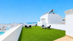 Eine Dachterrasse mit Kunstgrasanlage, Sitzgelegenheiten im Freien und Blick aufs Meer.