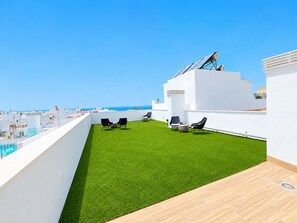 A rooftop terrace with artificial grass, outdoor seating, and a view of the sea. - Apartamento la Bodega con piscina (Conil de la Frontera)