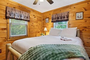 A wooden cabin bedroom with a bed, window with blinds, and a ceiling fan. - Hot Tub + Wraparound Decks + Arcade | Layered Ridge Views | Dream Chaser (Sevierville)