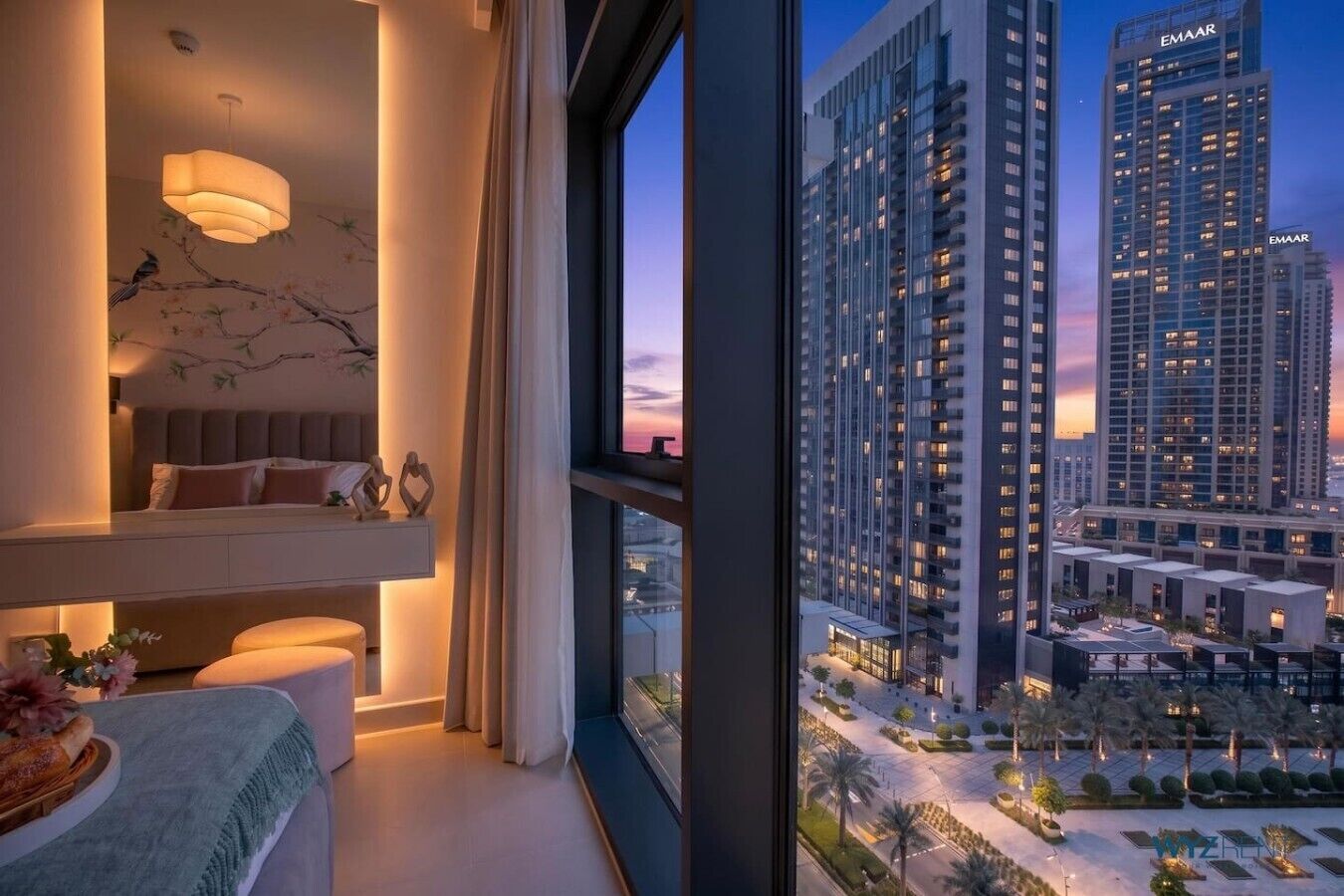 Una habitación de hotel moderna con un ventanal grande, una cama, una mesita de noche y un elemento decorativo en la pared.