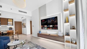 Una sala de estar moderna con un televisor de pantalla plana grande montado en la pared, un mueble bajo de madera y una zona de estar con un sofá azul y una mesa de centro.
