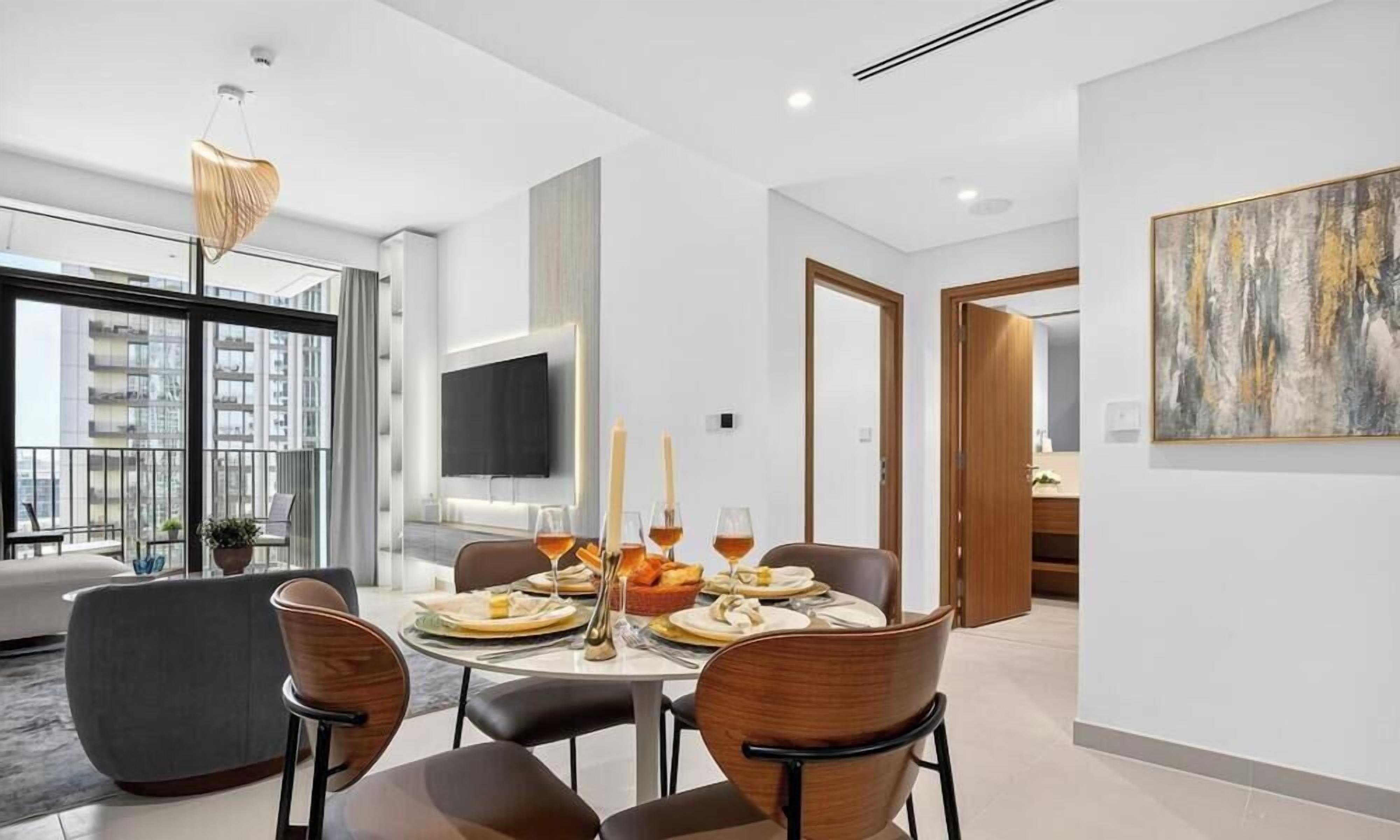 Un comedor moderno con una mesa redonda preparada para cuatro personas, un televisor de pantalla plana en la pared y un ventanal con vistas a la ciudad.