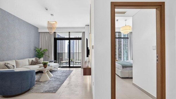 A modern living room with a sofa, coffee table, and a view of the city through large windows. - Feather & Stone 1BR | Creek Harbour skyline home (Dubai)