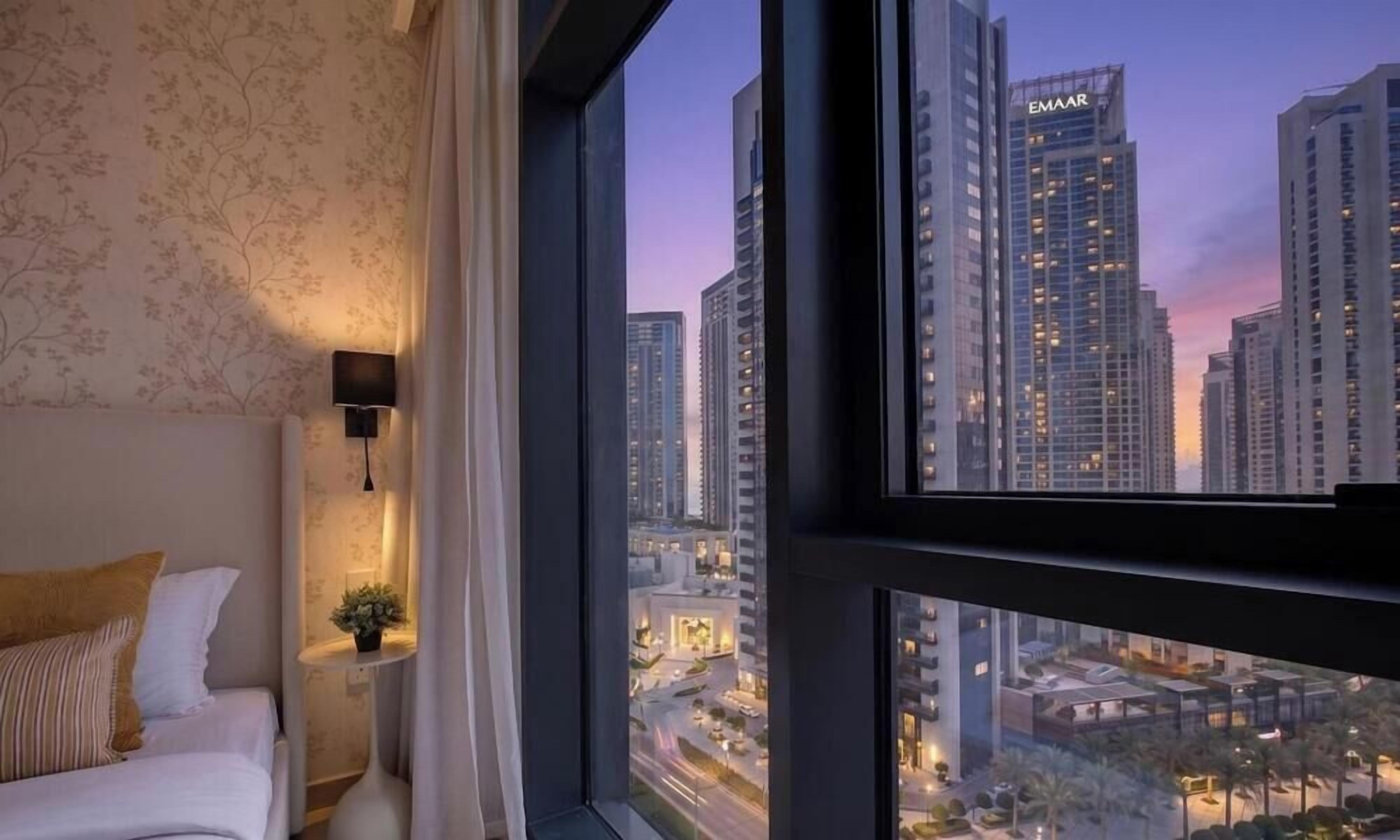 A hotel room with a large window, a bed, a nightstand, and a lamp.