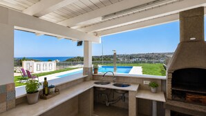 An outdoor kitchen with a view of the sea, a pool, and a grill. - Villa in Brucoli with 5 bedrooms sleeps 13 (Brucoli)