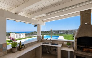 An outdoor kitchen with a view of the sea, a pool, and a grill. - Villa in Brucoli with 5 bedrooms sleeps 13 (Brucoli)