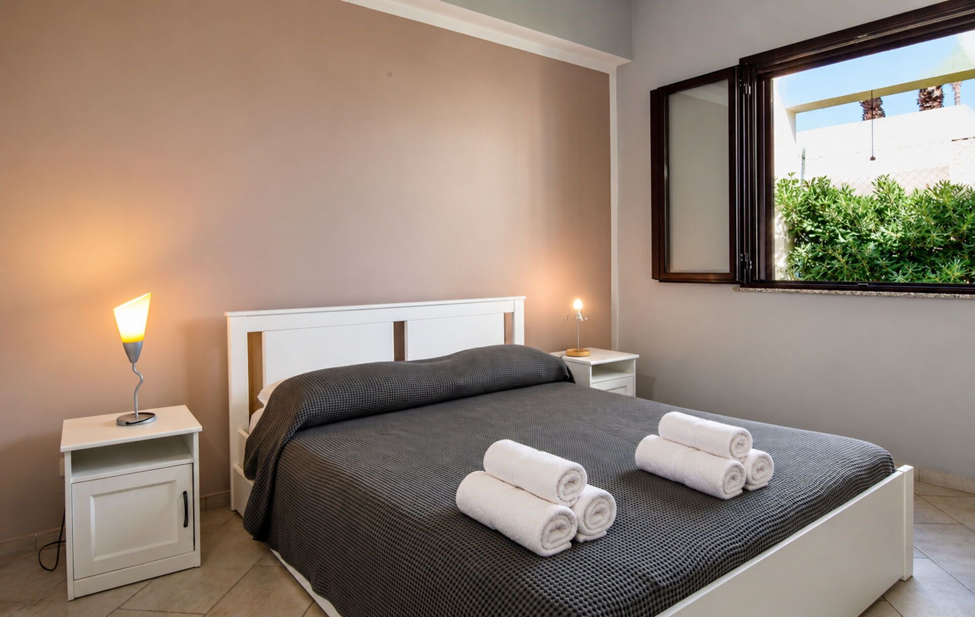 A bedroom with a bed, two bedside tables, a window with a view, and two lamps.
