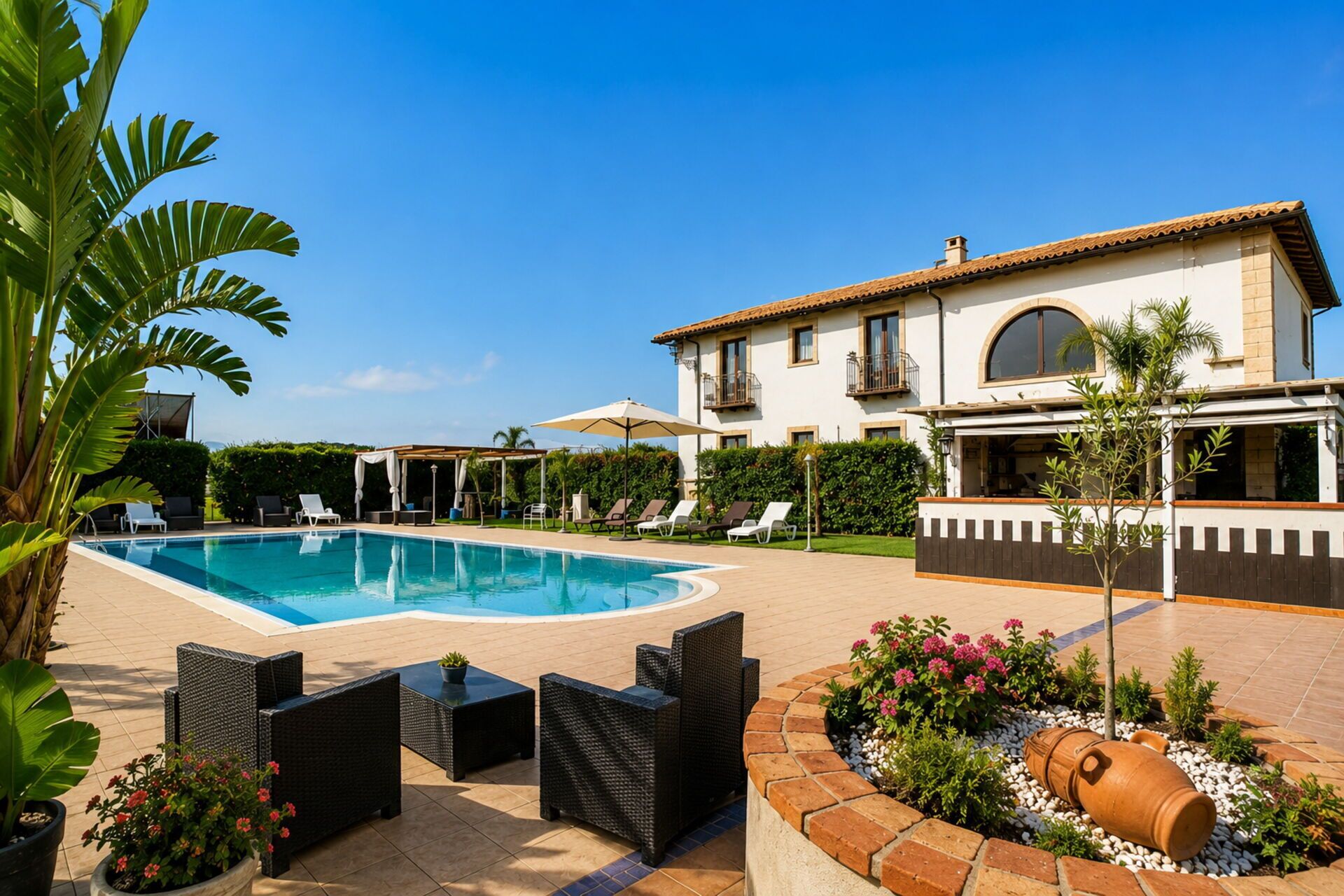 Une piscine avec des chaises longues, une pergola et une grande maison dotée d’un balcon.