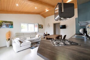 Une cuisine moderne avec un îlot central, un coin repas avec une table et des chaises en bois, un canapé et une grande fenêtre donnant sur une cascade.
