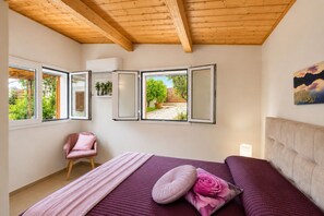 Une chambre à coucher avec un lit, une chaise et une vue sur l’extérieur par des fenêtres ouvertes.