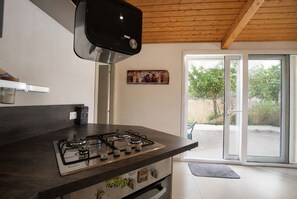 Une cuisine moderne dotée d’une cuisinière à gaz, d’un plafond en bois et offrant une vue sur l’extérieur grâce à une porte vitrée.