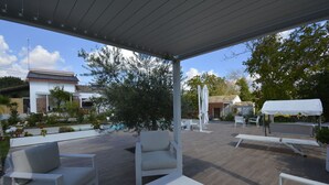 Eine Terrasse im Freien mit weißer Möbel, einem Grillplatz und Blick auf ein Haus im Hintergrund.