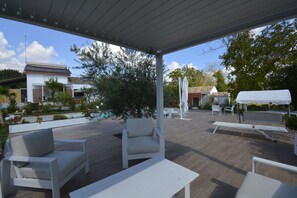 Eine Terrasse im Freien mit weißer Möbel, einem Grillplatz und Blick auf ein Haus im Hintergrund.