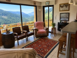 A cozy living room with a view of a mountainous landscape, a fireplace, and a dining area. - La Favellaz: Exceptional panoramic view of the Aravis mountain range and the village (Le Grand-Bornand)