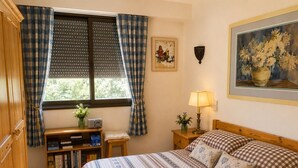 A bedroom with a bed, a bedside table with a lamp, a bookshelf, and a window with curtains. - La Favellaz: Exceptional panoramic view of the Aravis mountain range and the village (Le Grand-Bornand)