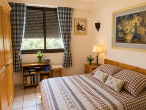 A bedroom with a bed, a bedside table with a lamp, a bookshelf, and a window with curtains. - La Favellaz: Exceptional panoramic view of the Aravis mountain range and the village (Le Grand-Bornand)