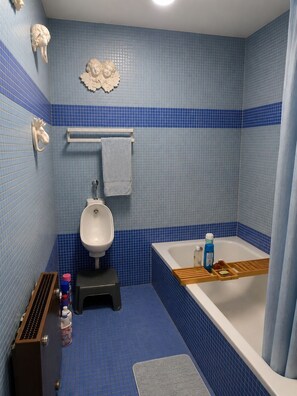 A bathroom with a white urinal, a bathtub with a wooden tray, and a blue tiled floor. - La Favellaz: Exceptional panoramic view of the Aravis mountain range and the village (Le Grand-Bornand)