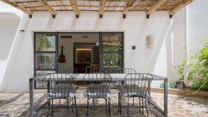 An outdoor patio with a table and chairs, a pergola overhead, and a view into the interior.