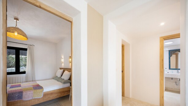Um quarto com cama, janela com cortinas, luminária de cabeceira e vista para o exterior.